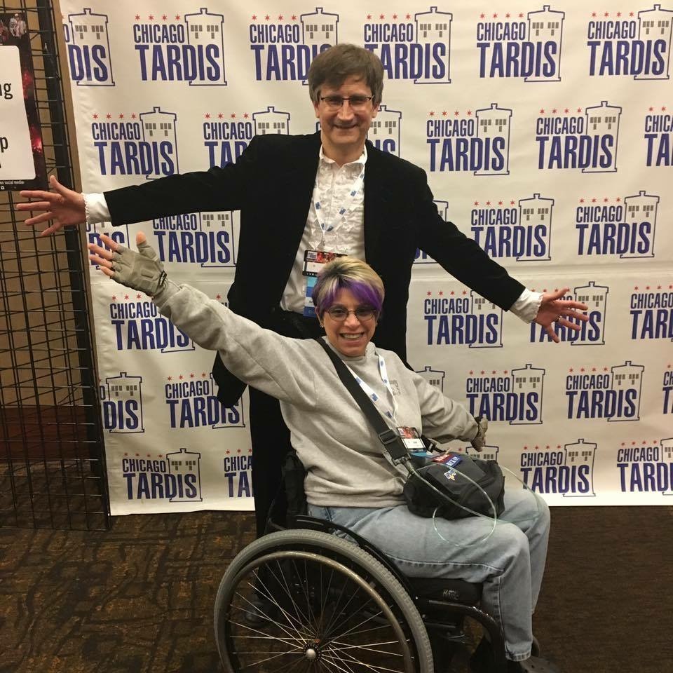 Woman in wheelchair and man standing behind, Chicago TARDIS backdrop behind