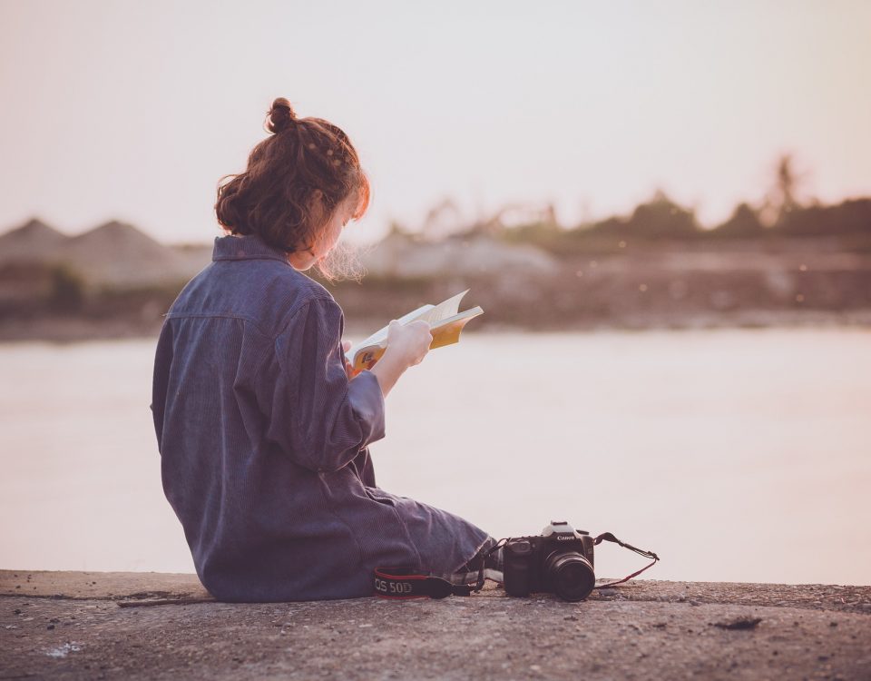 Woman with her back to camera reads a book on a boat dock at dusk